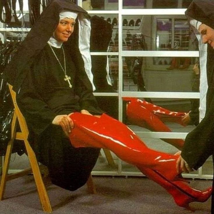 This may contain: two women in black robes and red boots are sitting on the floor with their feet propped up