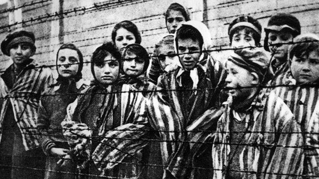A group of children standing behind a fence

Description automatically generated