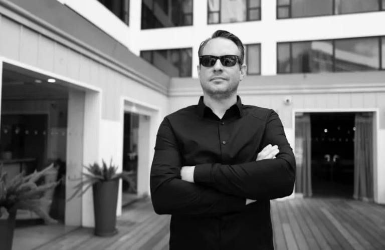 It's literally John Sparrow again, looking sharp in all black but this time he's standing in front of a hotel or something. Same sunglasses. This photo is horizontal, and the other one was vertical -- forgot to mention that. Also that one was in color, while this one is in black and white.