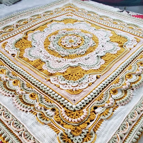 A crocheted mandala afghan blanket in goldenrod, sage, pink, and white.