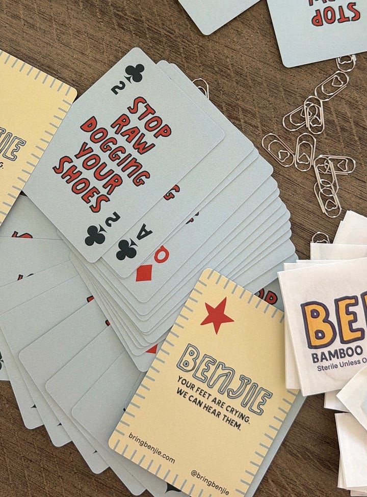 Two Coachella guerrilla marketing posters reading “Stop rawdogging your shoes,” with tear-off Benjie bandages attached—one on a bathroom  wall and one taped to a tree