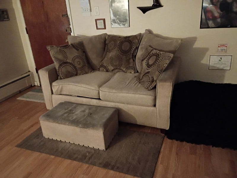 Beige couch that looks dirty  on pillows and top of ottoman