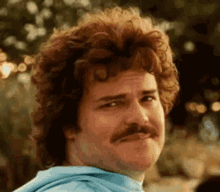 a man with curly hair and a mustache is wearing a blue shirt and making a funny face . a man with curly hair and a mustache is wearing a blue shirt and making a funny face .