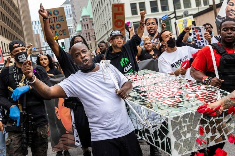Protesters carry a cardboard coffin down a city street Protesters carry a cardboard coffin down a city street
