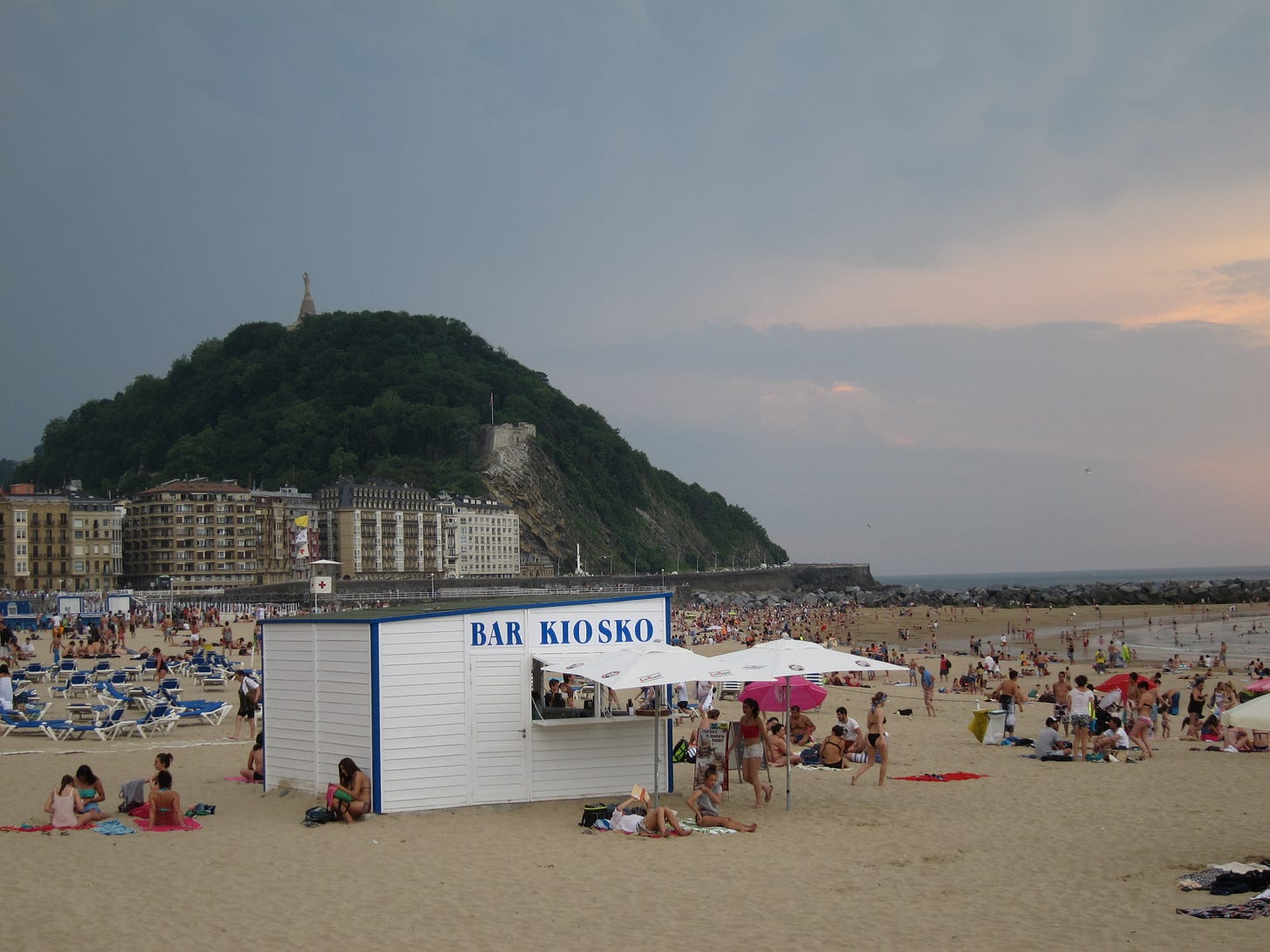 A beach and a bar with people and a big hill in the background