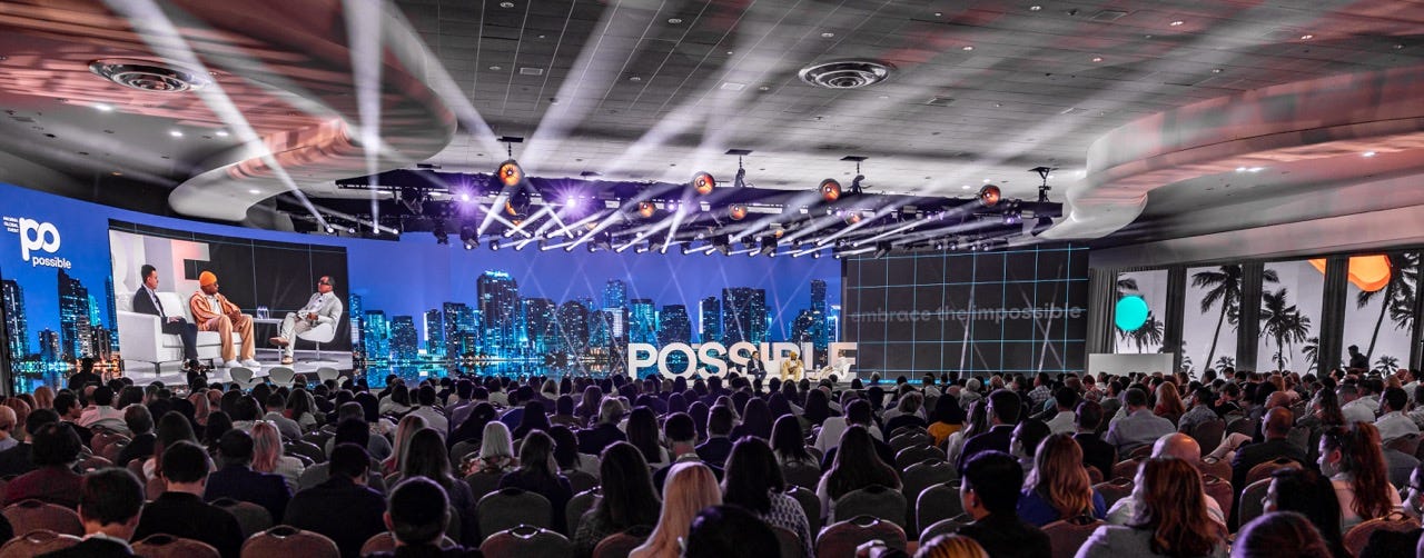 A group of people sitting in a room with a stage and lights

AI-generated content may be incorrect.