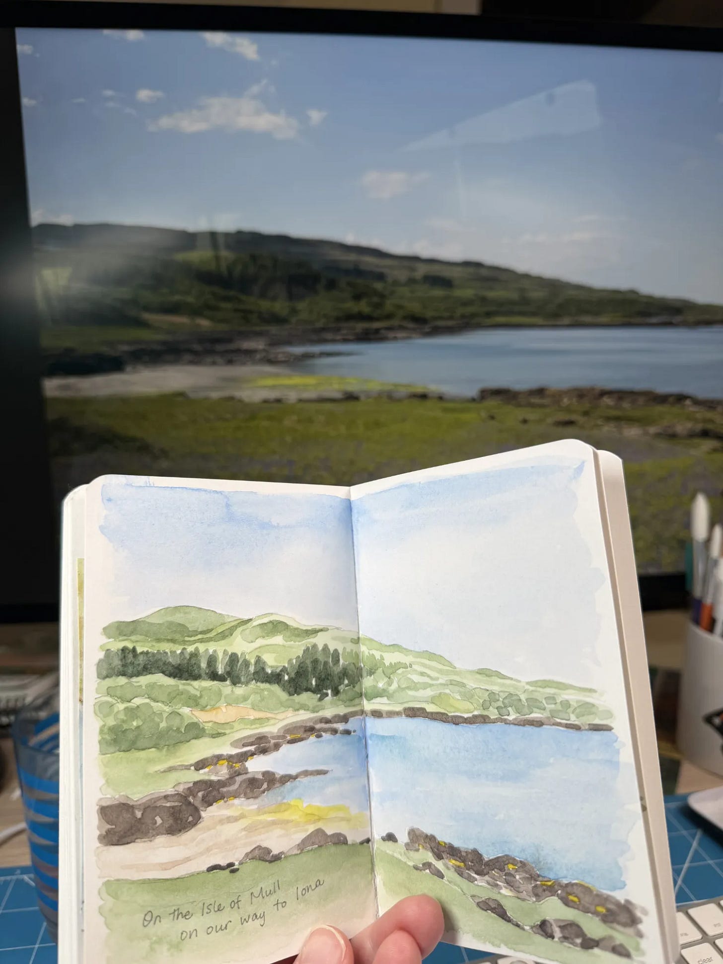 An open sketchbook with a background of the subject of the drawing, a landscape.