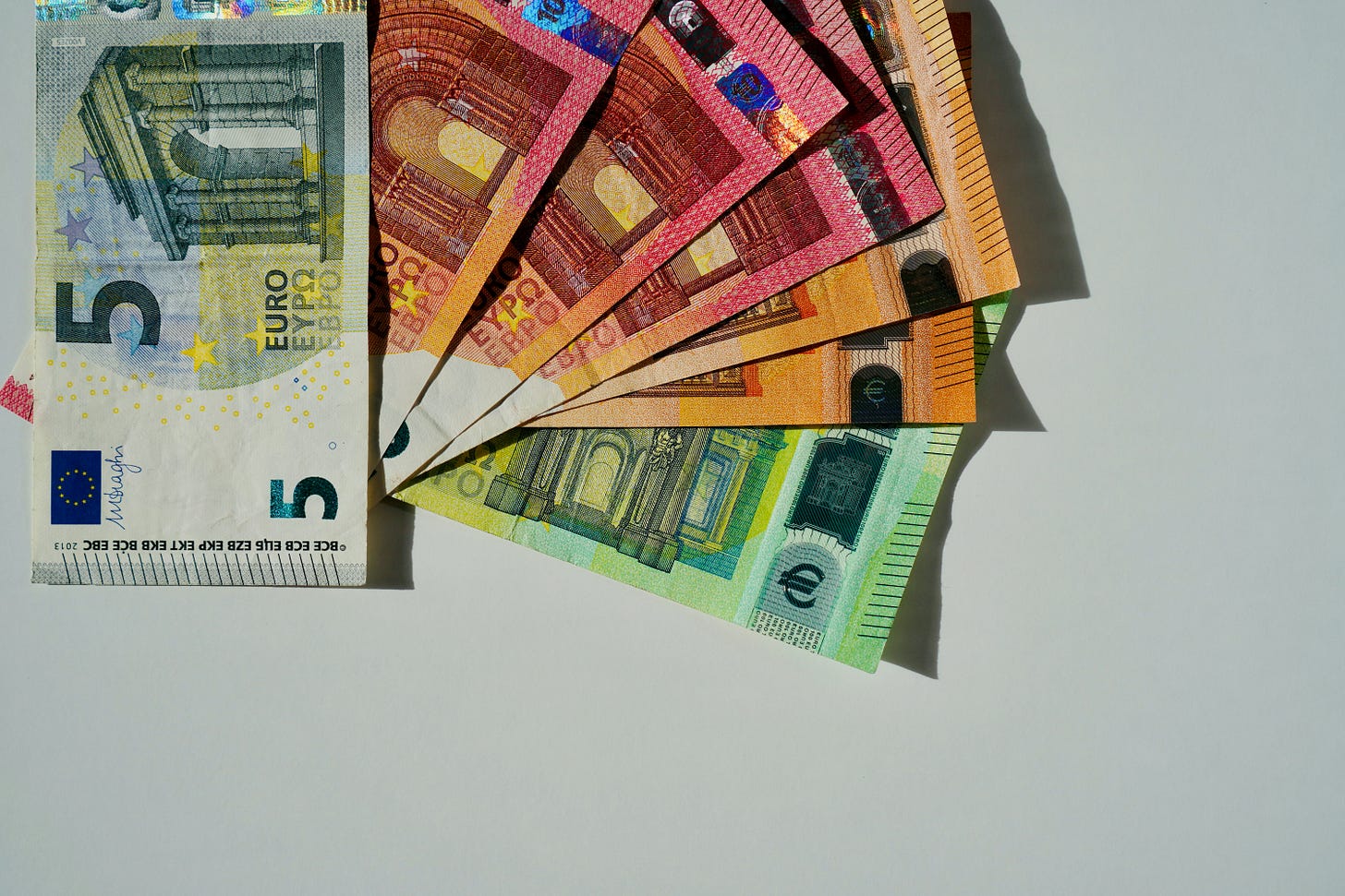 An image of six different denominations of Euro currency, fanned out against a neutral background