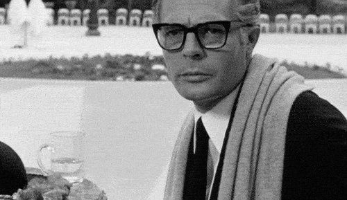 Animated gif of Marcello Mastroianni in 8½, seated with a scarf over his shoulder, gazing ahead with quiet reflection—symbolizing resigned introspection on a flawed but still valuable system.