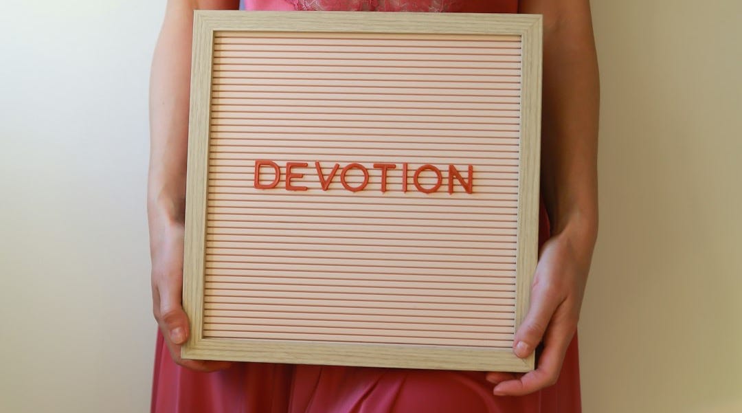 Woman in lingerie holding a sign that reads "devotion."