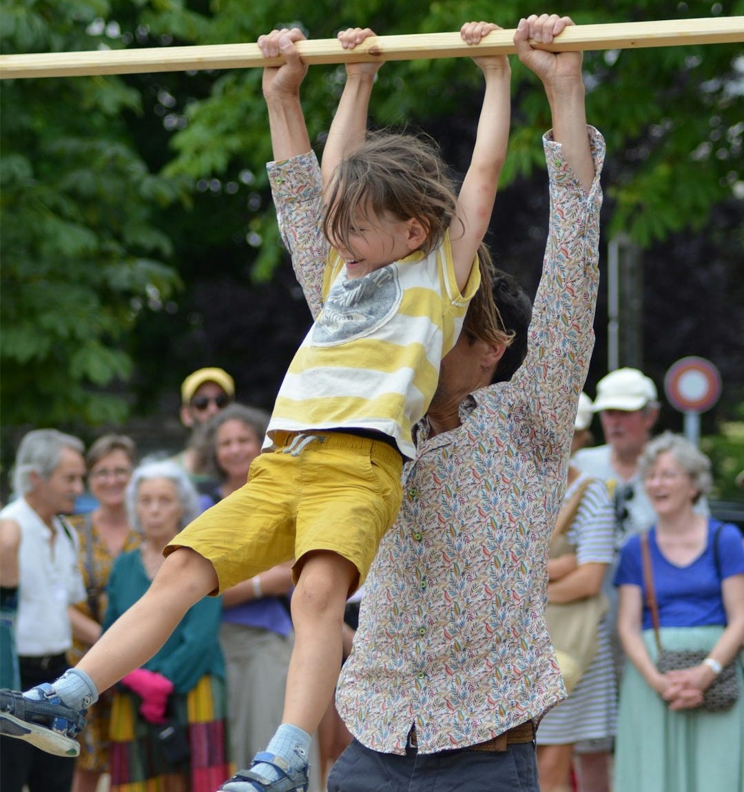 A man supports a boy hanging from a wooden bar.