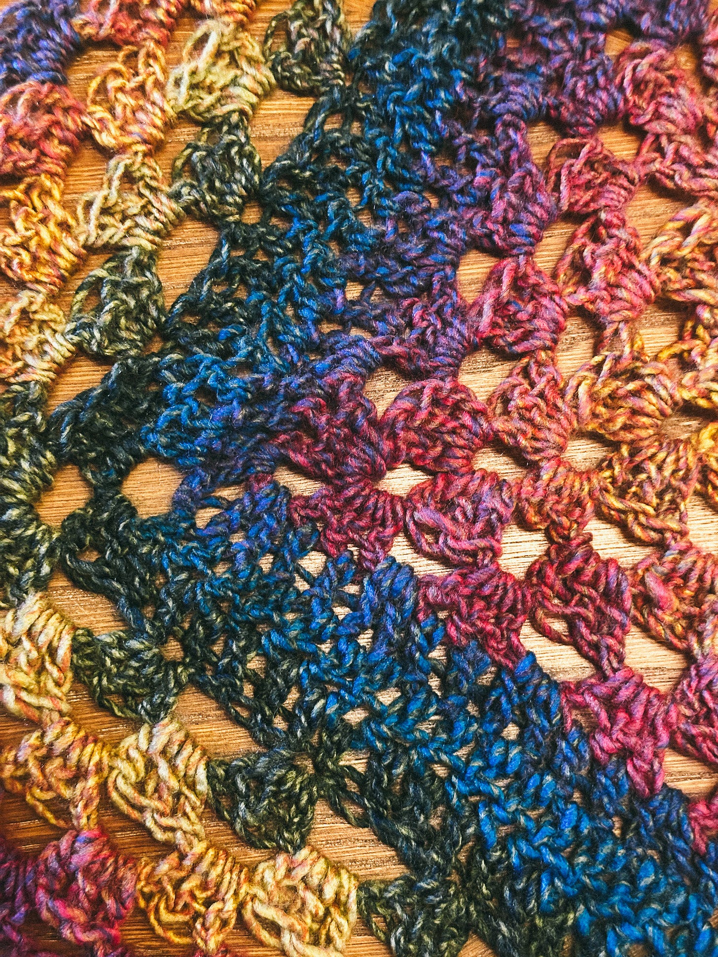 close-up of a shawl in rainbow yarn, alternating granny square rows with solid rows close-up of a shawl in rainbow yarn, alternating granny square rows with solid rows