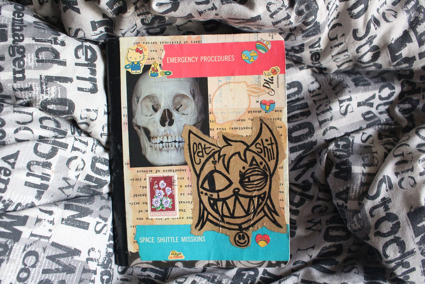 a colorfully collaged composition book with pictures of a skull, an illustrated grinning cat, stamps, a lemon, and hello kitty
