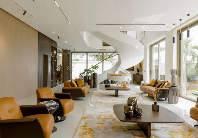 long living area with supple caramel colored leather swivel armchairs and pedestal tables and area rugs in light yellow and white and a white ceiling and glass doors and a swirly white spiral staircase at the far end long living area with supple caramel colored leather swivel armchairs and pedestal tables and area rugs in light yellow and white and a white ceiling and glass doors and a swirly white spiral staircase at the far end