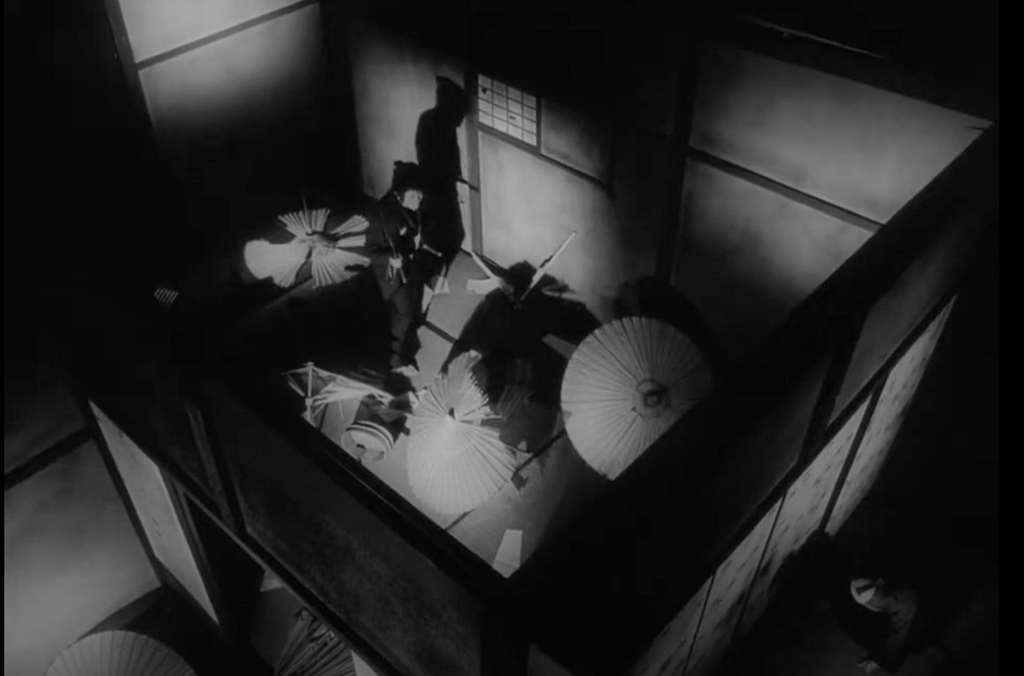 Film still from the 1971 movie “Demons/Shura”. A Birds Eye view in one room of a traditional Japanese home, where a lone samurai has his hand on his sheathed sword, as he surveys the carnage, broken paper umbrellas, and a corpse lay around him.