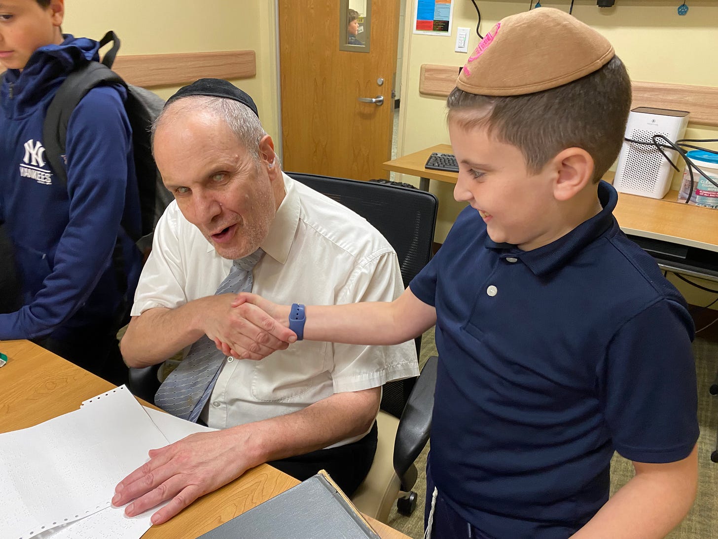 Rabbi Levy shakes the hand of an elementary school student who is smiling with excitement
