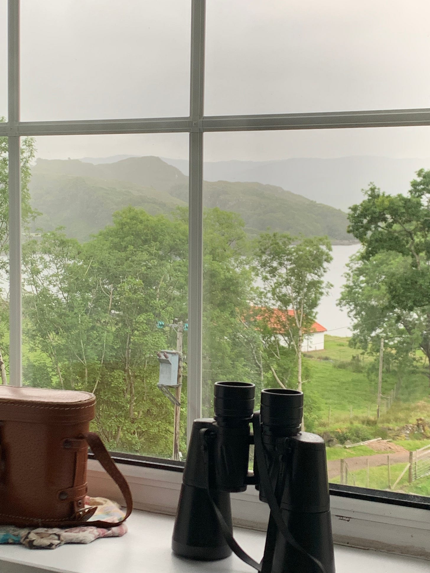 binoculars on a window sill by a window that is over looking a bay.