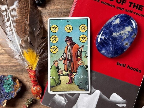 A tarot card lies on a wooden table. A book, crystal, feather and a bell surround it.