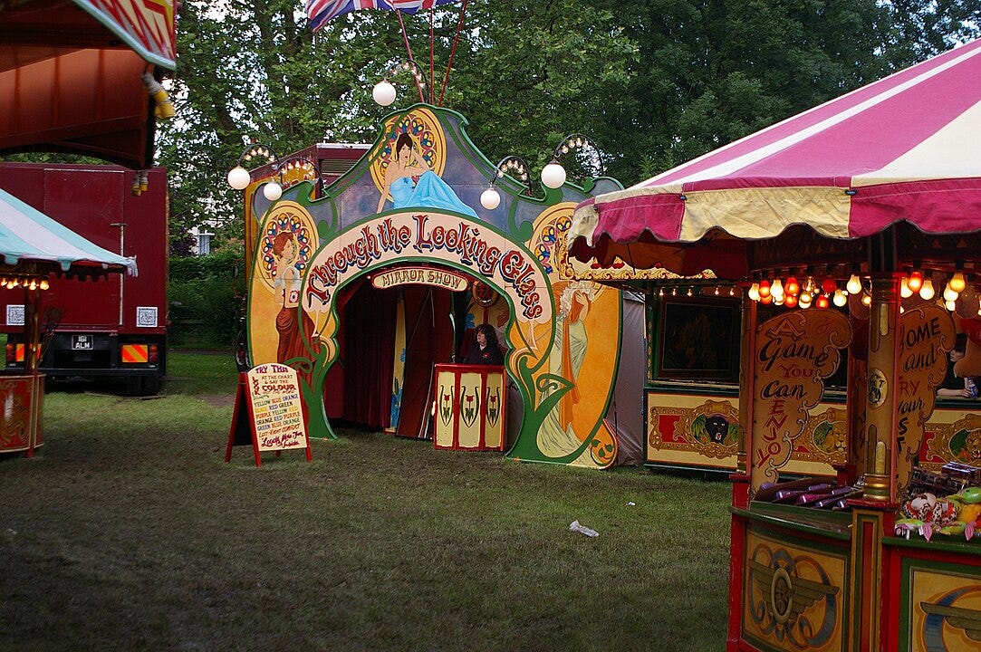 Photograph of a carnival, featuring a tent with the banner "Through the Looking Glass"