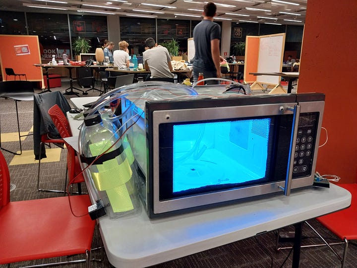 Images of a microwave modified to dispense drinks, one of which contains the author smiling beside the machine