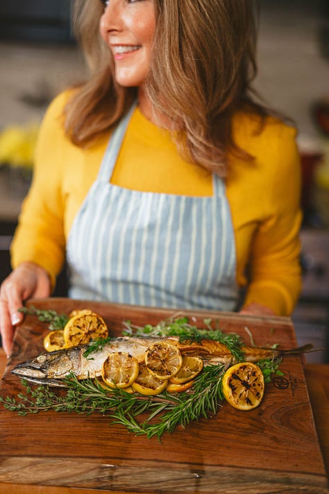 photos of fish almandine on a platter, seafood risotto in a white bowl, Karista pouring a seafood boil onto a plastic tablecloth, Karista holding a whole roasted fish, salmon with brown butter pasta with peas and mint and a crispy fish burger with special sauce sitting on a wooden board