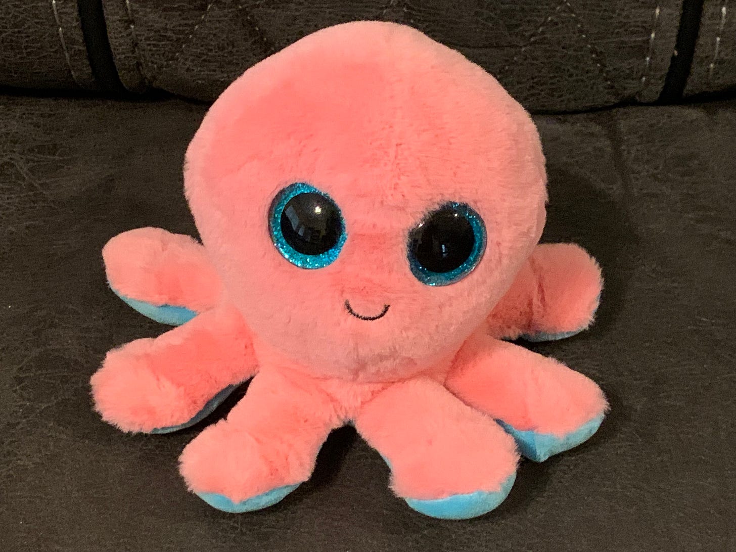 Smiling pink octopus stuffed animal with large blue eyes