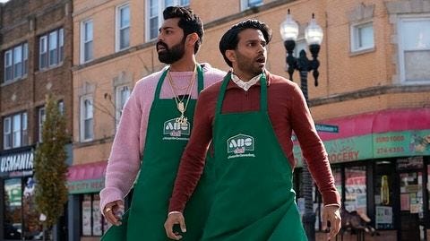 This may contain: two men in green aprons walking down the street