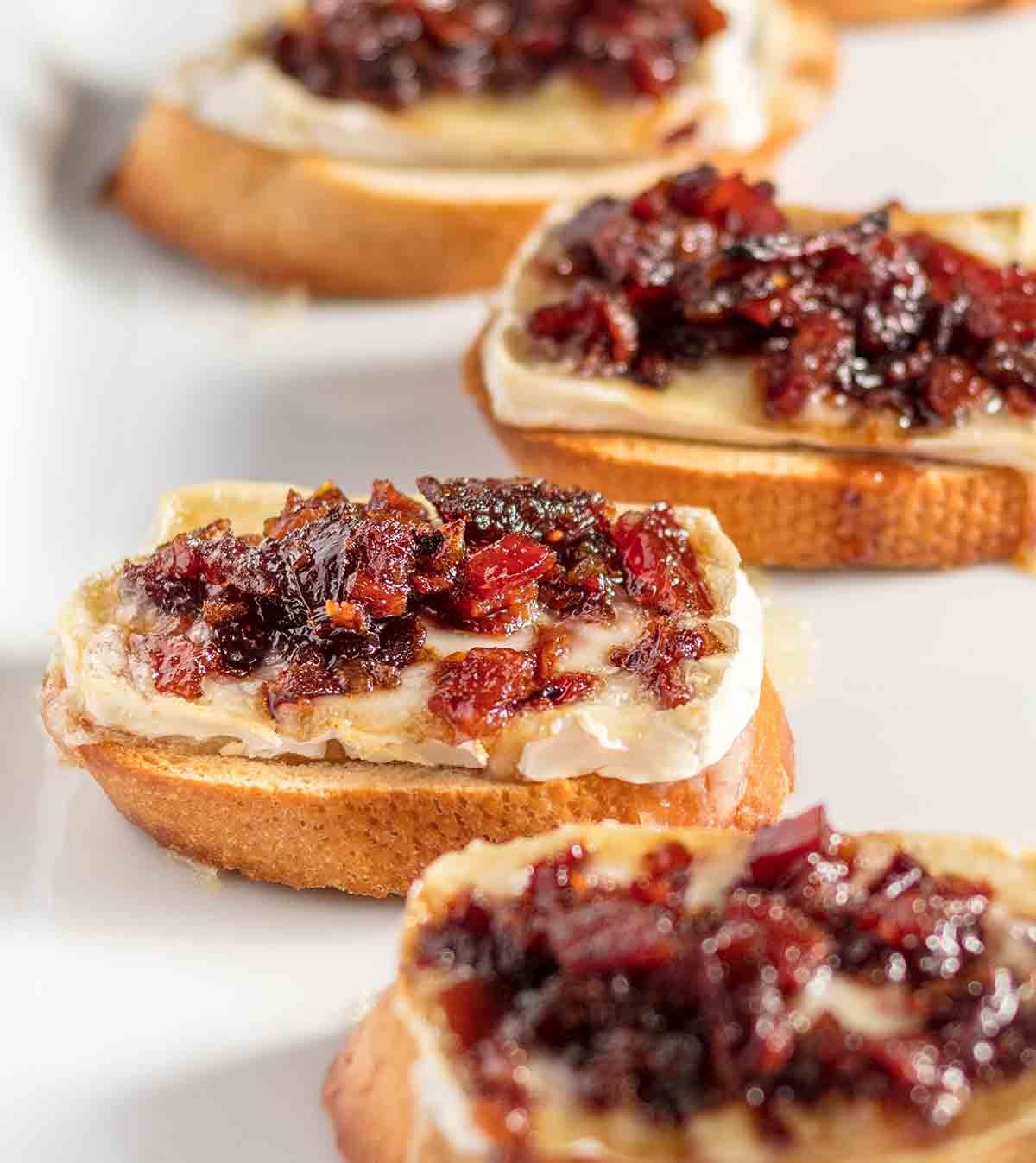 Crostini with a slice of brie cheese topped with glistening bacon jam.
