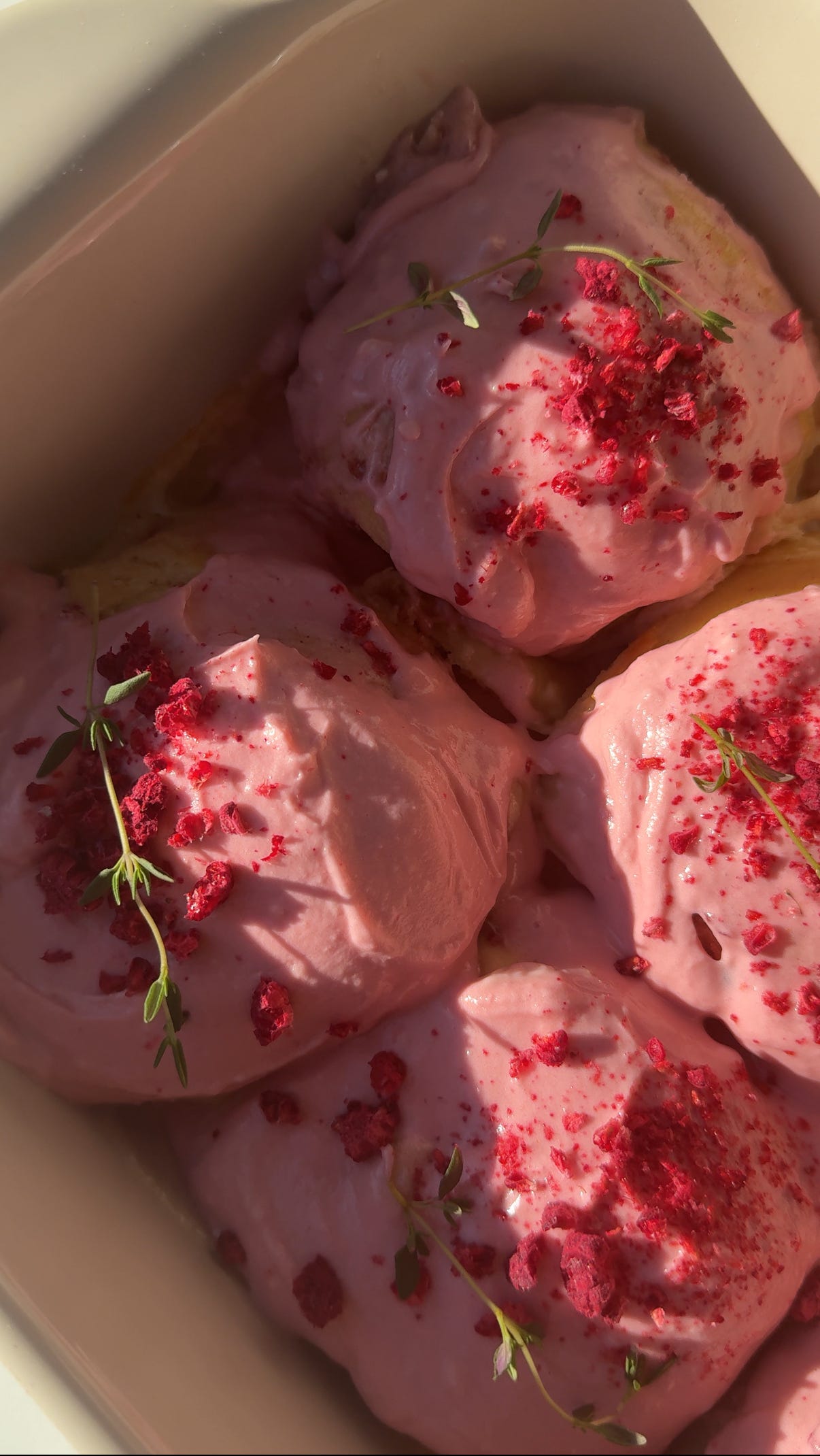 pink raspberry almond sweet rolls in a baking pan with raspberry cream cheese frosting and crushed freeze dried raspberries on top