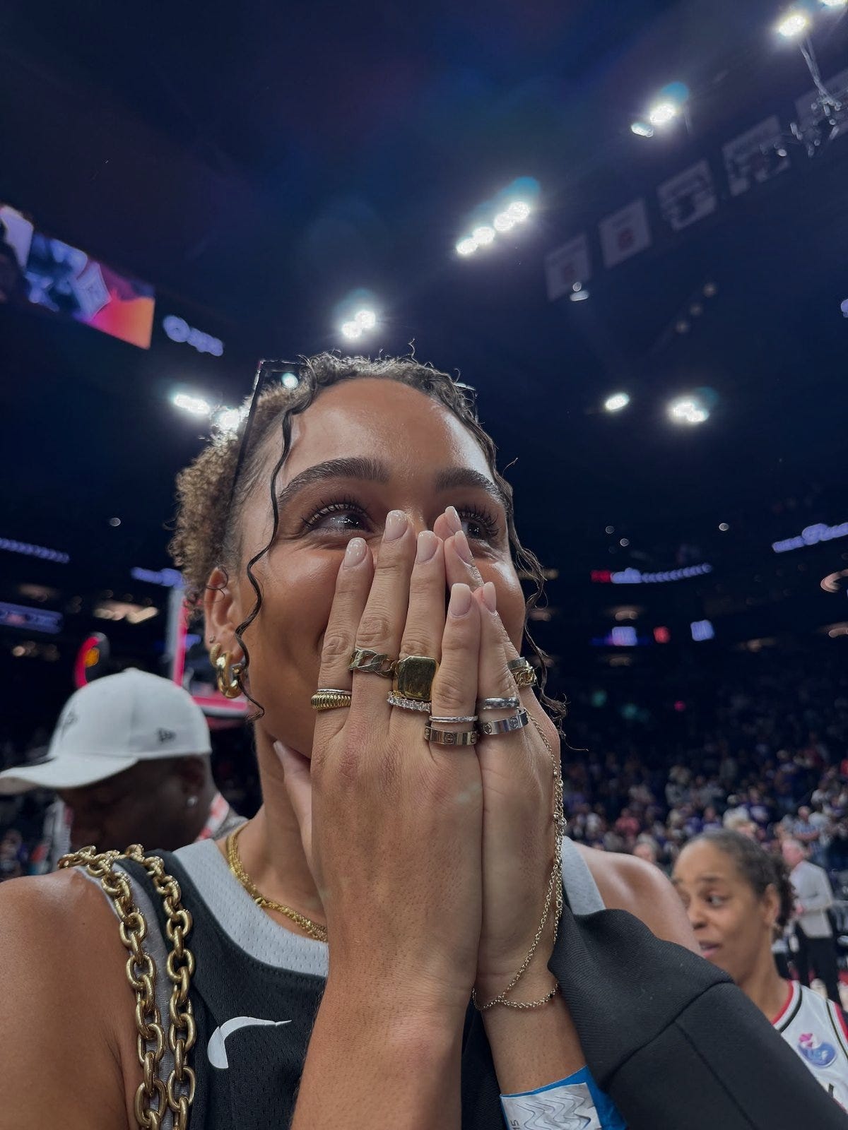 Excited fan with stacked rings and gold jewelry covering her face in disbelief at a WNBA game Excited fan with stacked rings and gold jewelry covering her face in disbelief at a WNBA game
