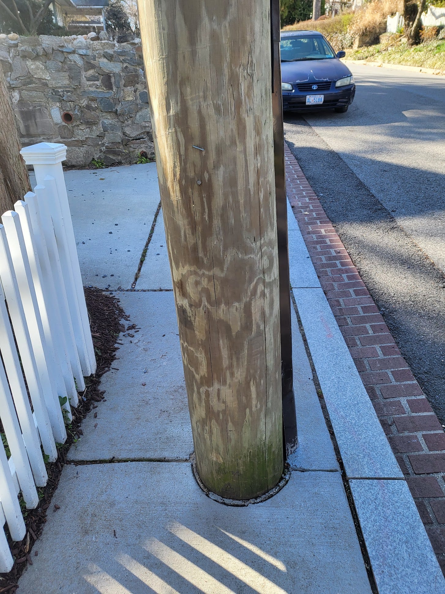 Picture shows a utility pole in the middle of the sidewalk. On the right side, Newark St. NW is seen with the opposite side of the street showing no sidewalk.