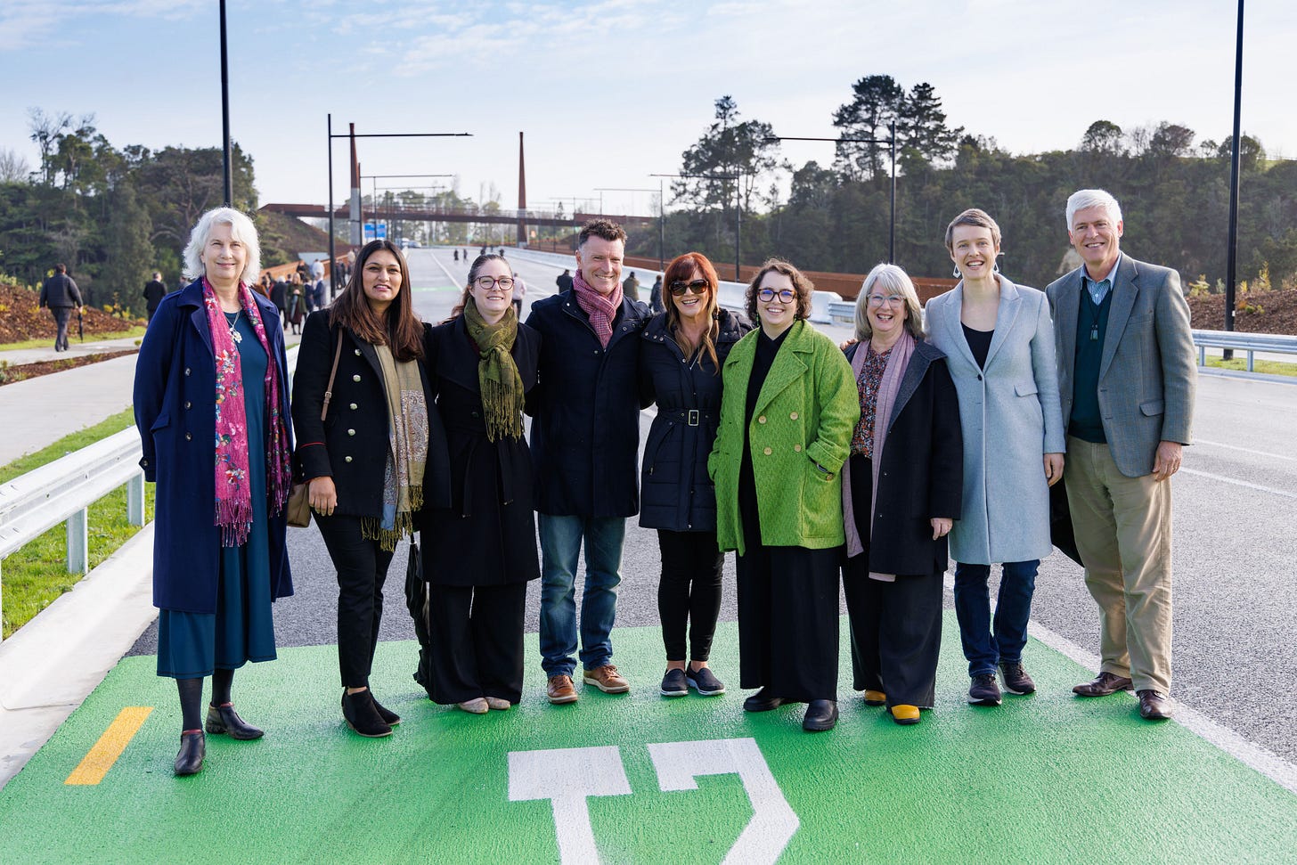 From left to right, Mayor Southgate and Crs Naidoo-Rauf, Pike, Donovan, Deputy Mayor O'Leary, Crs Hutt, van Oosten, Thomson, and Macindoe, standing in winter coats and jackets, on the carriageway of the new bridge in Kirikiriroa Hamilton. They're all smiling at the camera.
