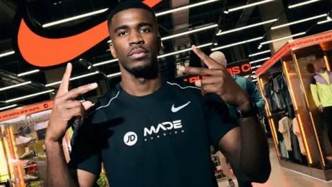 Hermen Dange Hermen Dange hold up his arms while he poses in a black t-shirt outside a shop Hermen Dange Hermen Dange hold up his arms while he poses in a black t-shirt outside a shop