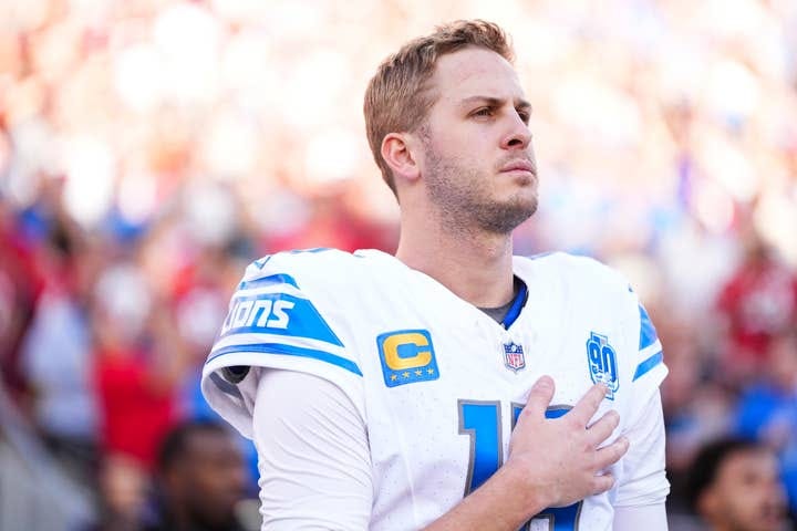 Football player in uniform with captain's "C" patch stands solemnly on the field during a game