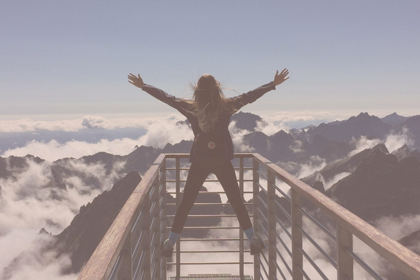 Woman on top of a mountain, arms stretched wide 
