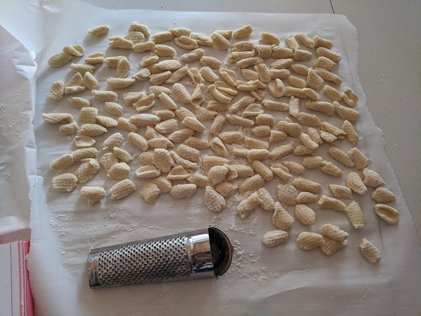 a large piece of parchment covered in hand-formed small pasta shapes, rolled across a nutmeg grater for texture