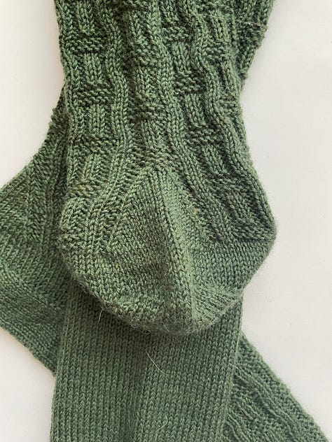 A green hand knit sock with a basket weave pattern.