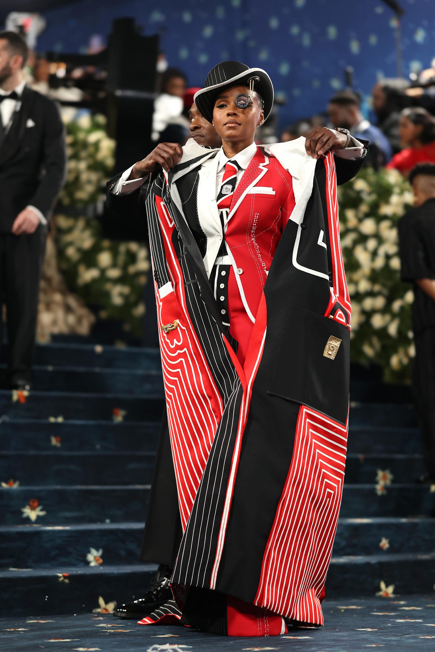 Janelle's suit overcoat is removed, revealing a second red, black and white suit underneath on the Met steps.