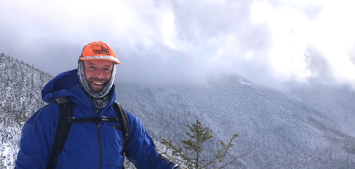 Jesse McEntee smiling in a blue jacket on a snowy mountain ridge.