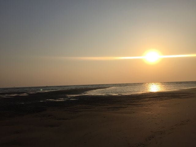 A sunset on an ocean. The sky is gold and grey. The sun reflects on the water. The sand shines like gold. A sunset on an ocean. The sky is gold and grey. The sun reflects on the water. The sand shines like gold.