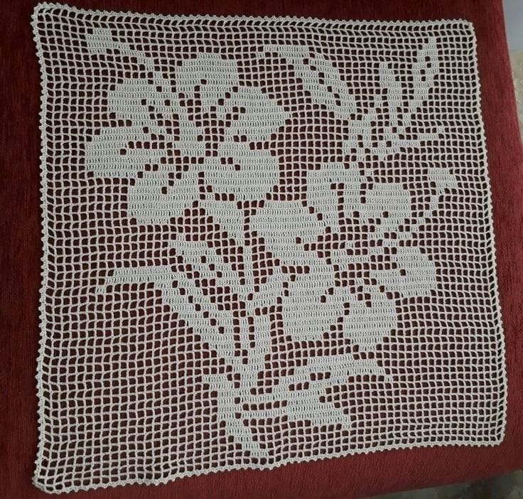 This may contain: a red pillow with white crocheted flowers on it