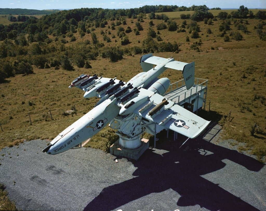 An A-10 Thunderbolt II aircraft is mounted on a pedestal during a test at the Rome Air Development Center's Newport Test Site, July 1984. Cluster bombs and an electronics countermeasures pod are mounted on the aircraft's pylons. <em>National Archives</em>