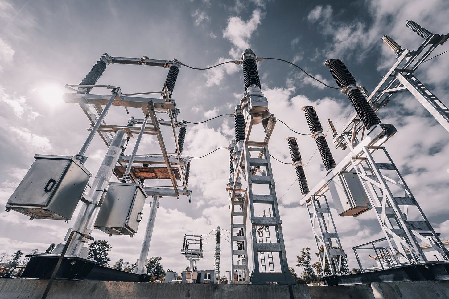 High-voltage substation equipment seen from below against a cloudy sky