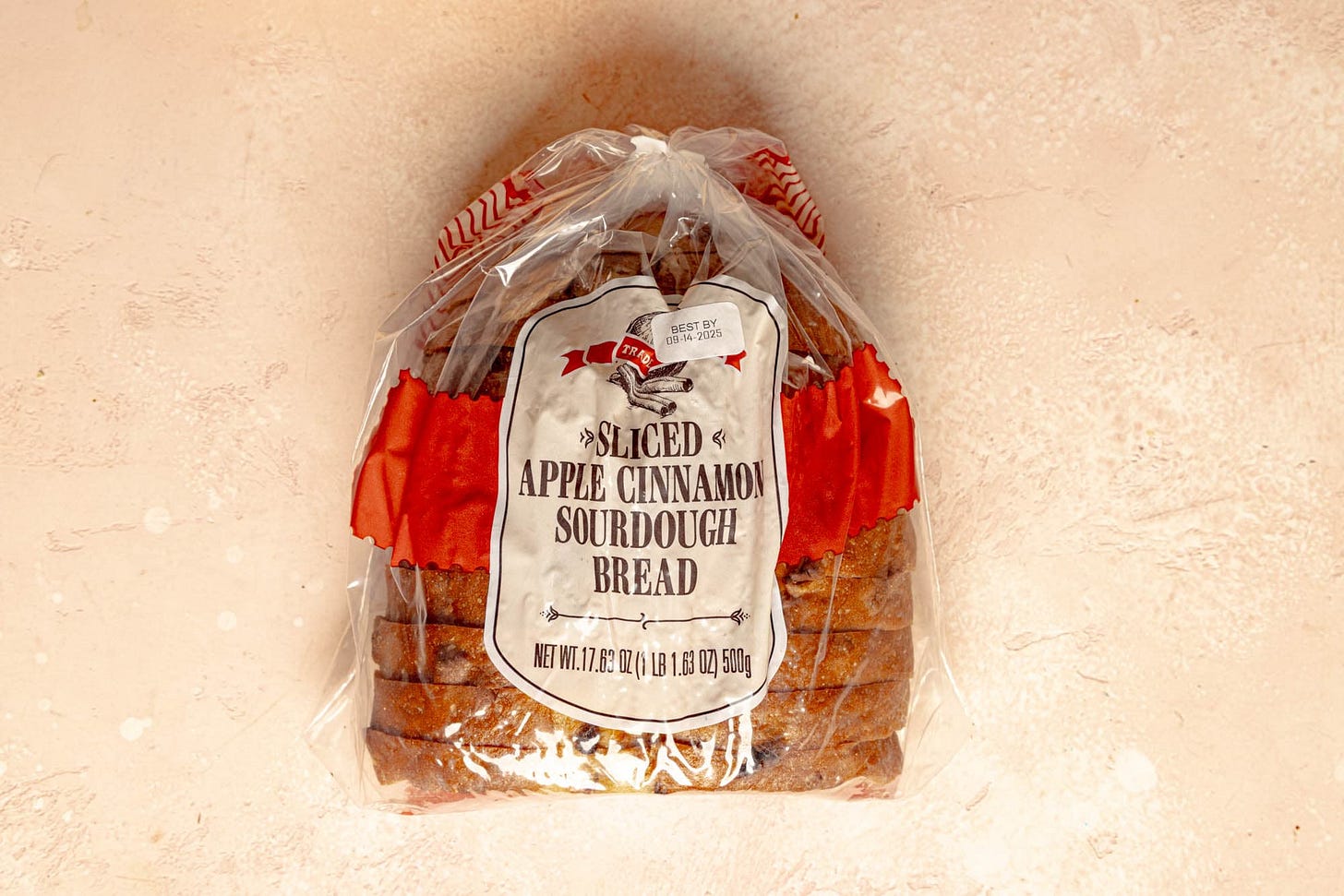An unopened package of Trader Joe's Sliced Apple Cinnamon Sourdough Bread on a pink surface.