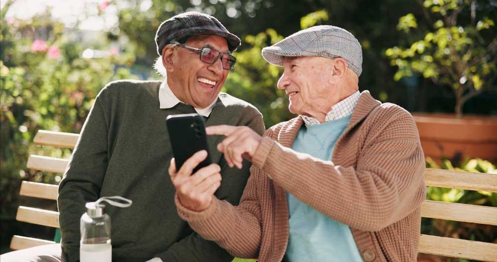 Pensioner old friends laughing together outside on a park bench.