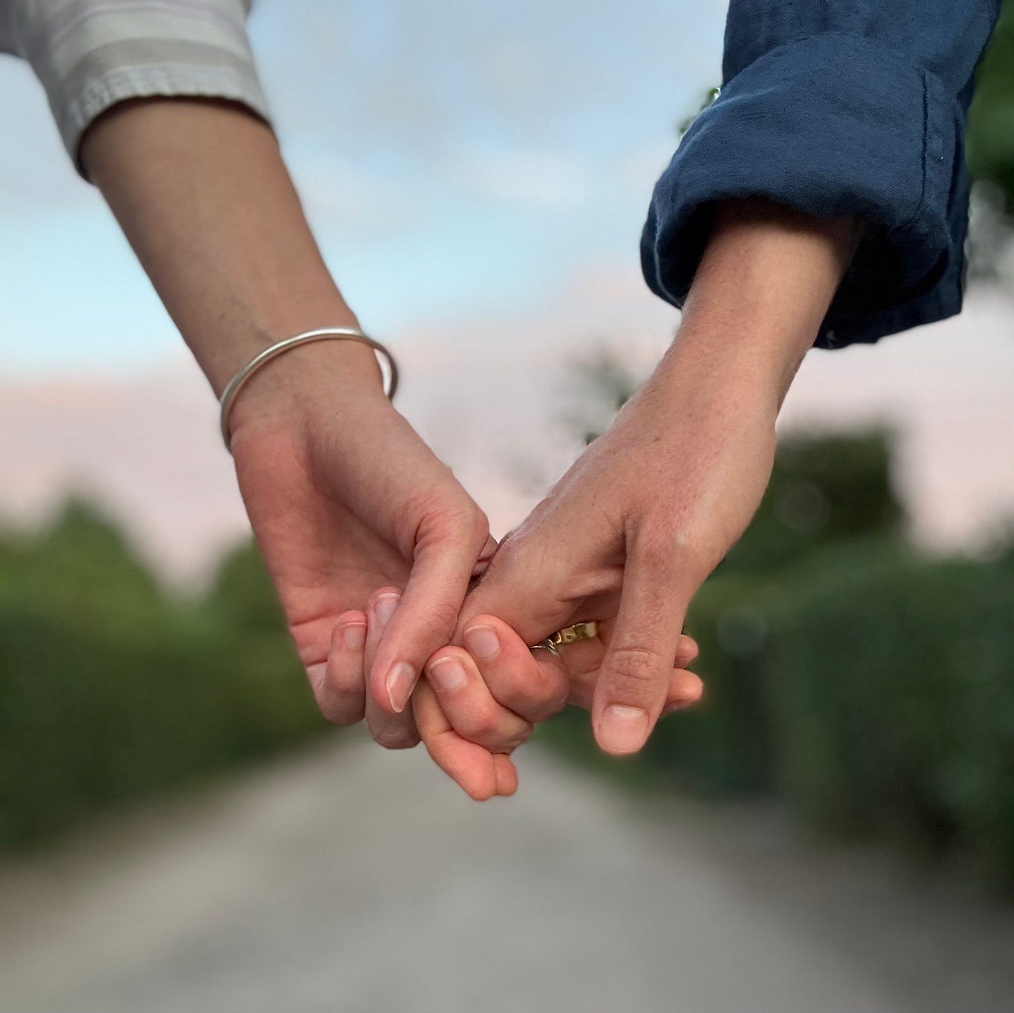 An image of two people holding hands by their two forefingers, a soft pink sky in the background. An image of two people holding hands by their two forefingers, a soft pink sky in the background.