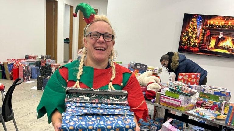 A Mothershare elf holding a wrapped present. A Mothershare elf holding a wrapped present.