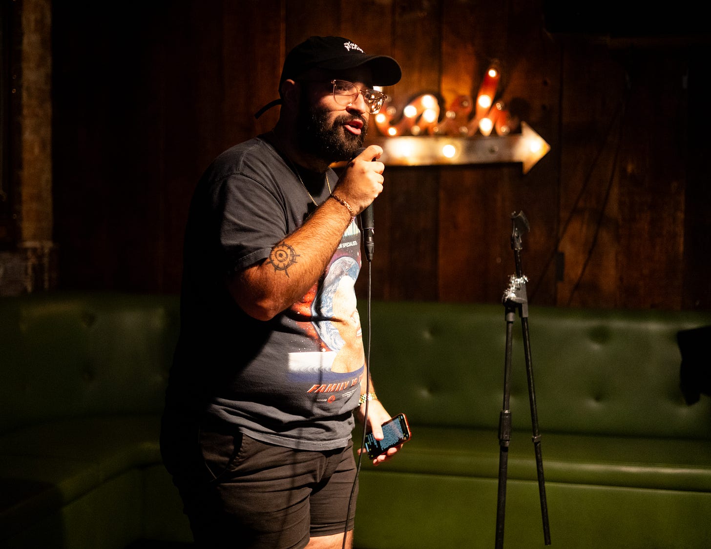 Julian Hernandez performs holding mic wearing glasses and black baseball cap at queers n peers variety show