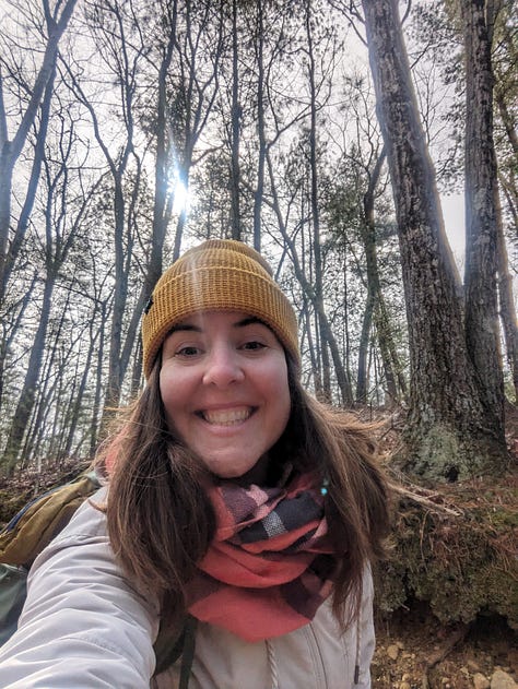 Three images. The first is myself in a yellow knit hat in a forest facing down toward the camera with trees and sunlight on Walden Pond. The middle image is The Bookhive logo, which is a stack of books in the shape of a hive with the words underneath. The third image is looking down towards my green shoes with a white book painted on a paved walkway.