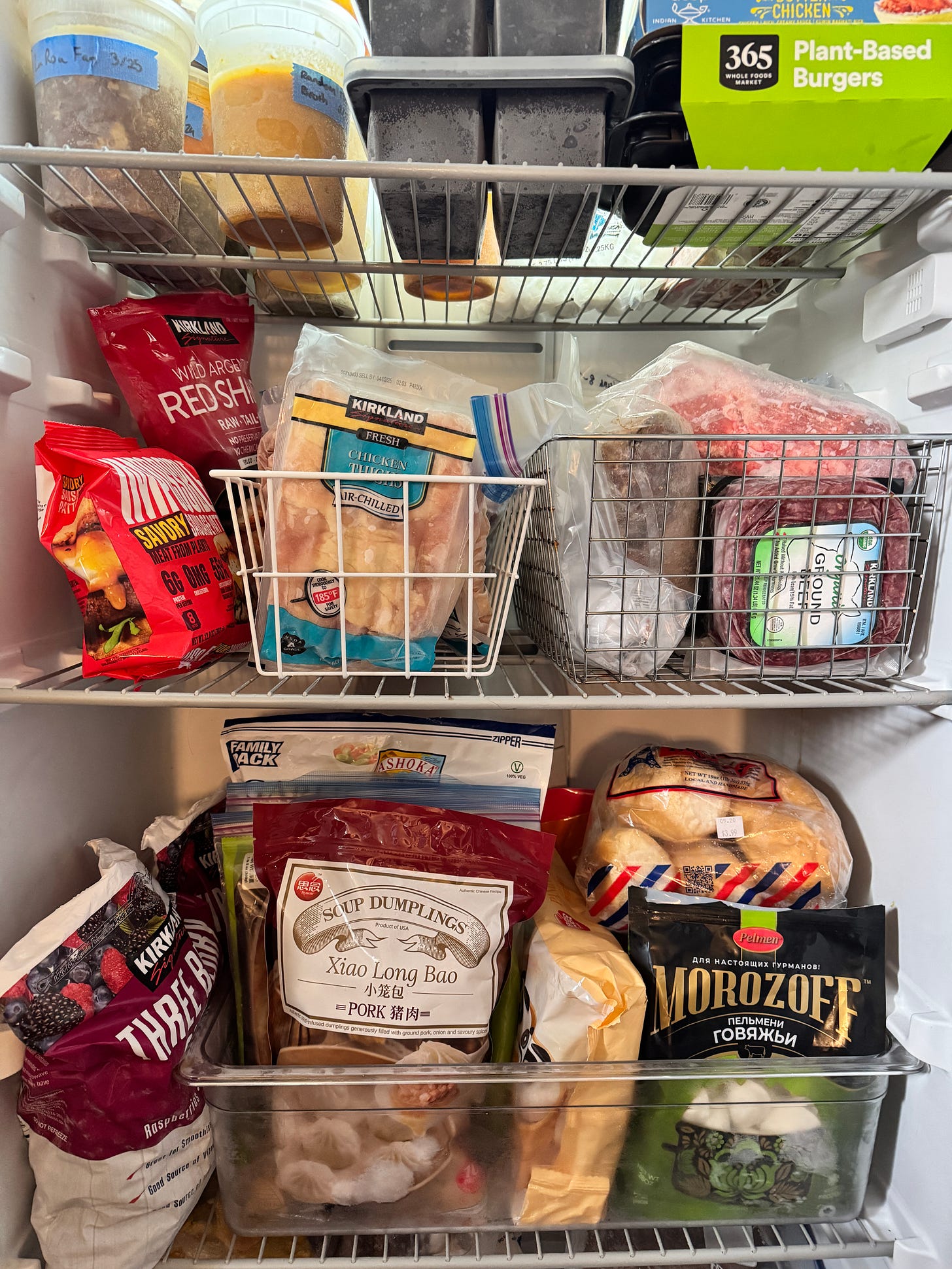 A view of the inside of a freezer, showing plastic quart containers of stock, packages of ground beef and chicken thighs, frozen fruit, and dumplings.
